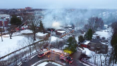 A-snowy-suburban-neighborhood-school-is-on-fire,-and-firefighters-distinguish-the-fire