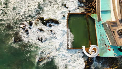 Top-down-drone-shot-of-waves-hitting-a-pool-and-a-waterslide-in-Mazatlan,-Mexico