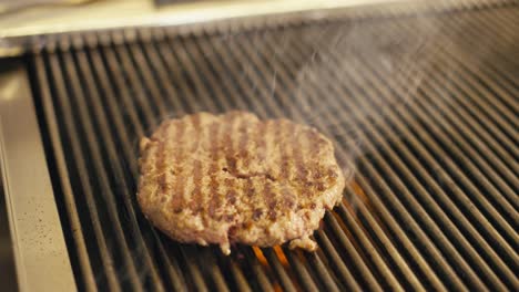 Hamburguesa-Jugosa-Chisporroteando-En-La-Parrilla-Con-Vapor-Subiendo,-Primer-Plano,-Ambiente-Interior