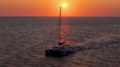 Aerial-frontal-orbit-around-catamaran-driving-across-open-ocean-at-sunset