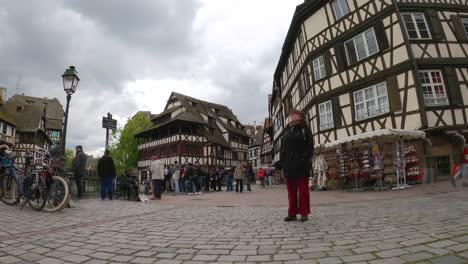 Gente-Caminando-Por-La-Calle-En-Place-Benjamin-Zix-Con-Tienda-De-Souvenirs-En-Petite-France,-Estrasburgo,-Francia