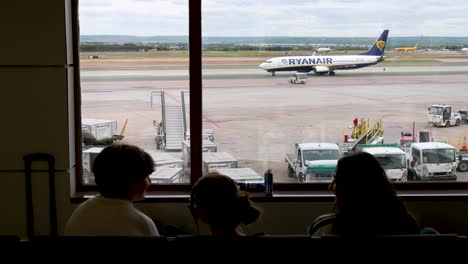 Los-Pasajeros-Del-Vuelo-Están-Sentados-En-La-Zona-De-Espera-Como-La-Aerolínea-De-Bandera-De-La-Aerolínea-Irlandesa-De-Bajo-Coste-Ryanair.-Taxis-En-La-Pista-Del-Aeropuerto-Adolfo-Suárez-De-Madrid-Barajas-En-Madrid,-España.