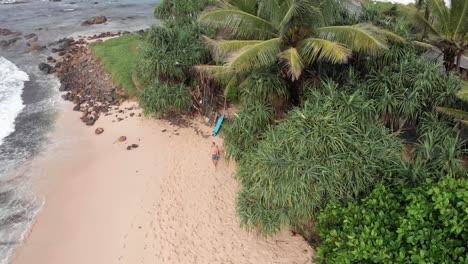 Man-Walking-Along-Beach-and-Placing-Down-Surfboard-in-Sand