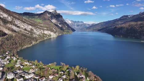 Aerial-view-of-Weesen,-showcasing-the-azure-waters-of-Walensee,-surrounded-by-vibrant-greenery-and-nestled-against-towering-mountains