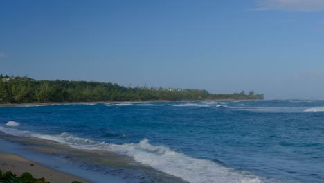 Static-clip-of-waves-crashing-on-a-Puerto-Rican-beach,-looking-out-at-a-point-with-tropical-trees-and-sand