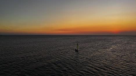 Einsames-Segelboot,-Das-Während-Eines-Spektakulären-Sonnenuntergangs-In-Der-Dämmerung-über-Das-Ruhige,-Friedliche-Wasser-Der-Bucht-Von-Mui-Ne-Kreuzt