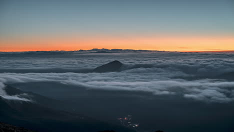 Majestätisches-Wolkenmeer-Im-Morgengrauen-Mit-Einem-Einsamen-Gipfel-Darüber,-Darunter-Funkelnde-Lichter-Der-Stadt