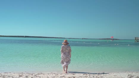 Mujer-Con-Sombrero-Y-Vestido-Camina-Hacia-El-Hermoso-Mar-Lento-Backshot