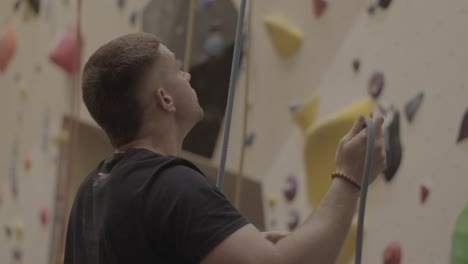 Man-securing-rope-at-indoor-climbing-facility,-climber-preparing-gear-in-gym