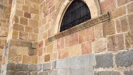 Vemos-Un-Lateral-De-La-Iglesia-De-San-Nicolas-Donde-Aparece-Una-Antigua-Puerta-Cerrada-Y-Convertida-En-Ventana-Con-Una-Bonita-Decoración-Y-Aparece-Un-Pequeño-Ojo-De-Buey-En-La-Parte-Superior