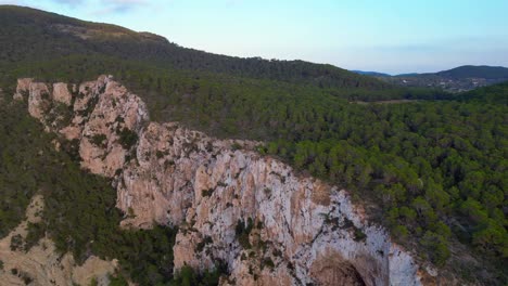 Hikers-rest-on-a-rocky-cliff-among-trees-with-a-view-of-the-green-landscape-during-sunset-in-ibiza