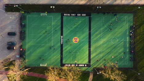 Antena-Arriba-Hacia-Abajo-De-Personas-Jugando-Fútbol-Y-Baloncesto-En-Tres-Campos-Deportivos-Verdes-Durante-La-Puesta-De-Sol