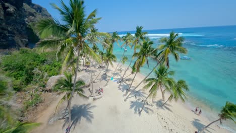 Fpv-drone-flight-over-sandy-beach-with-palm-trees,-following-fast-speedboat-on-Caribbean-Sea