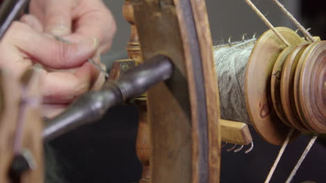 Through-spokes-of-traditional-spinning-wheel,-hands-pull-wool-for-yarn