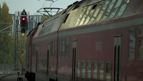Red-Deutsche-Bahn-train-approaching-a-station-platform-on-a-cloudy-day,-man-waiting,-urban-backdrop