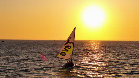 Kleines-Segelboot-Nähert-Sich-Dem-Meereshorizont-Während-Eines-Spektakulären-Sonnenuntergangs-Zur-Goldenen-Stunde
