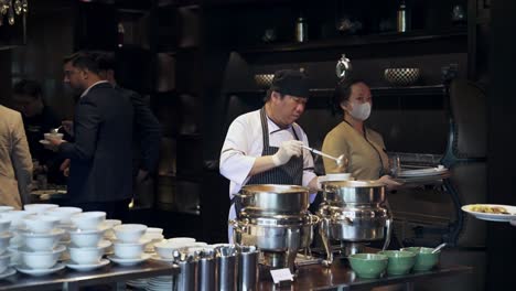 Chef-Asiático-Ocupado-Preparando-Comida-En-La-Cocina-De-Un-Restaurante-Humeante,-Centrado-En-Su-Tarea