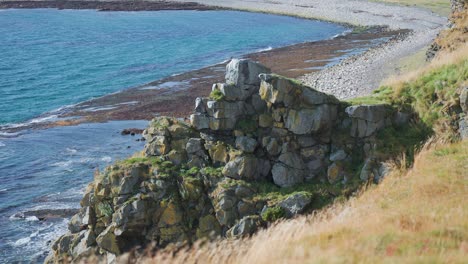 Soft-grass-covers-the-towering-withered-cliffs-above-the-coast,-while-waves-crash-onto-the-beach