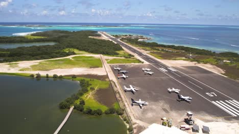 Los-roques-airstrip-with-planes,-one-landing,-tropical-backdrop,-aerial-view