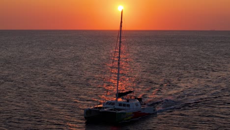 Catamaran-bounces-as-it-glides-across-Caribbean-waters-glowing-red-from-golden-hour-sunset
