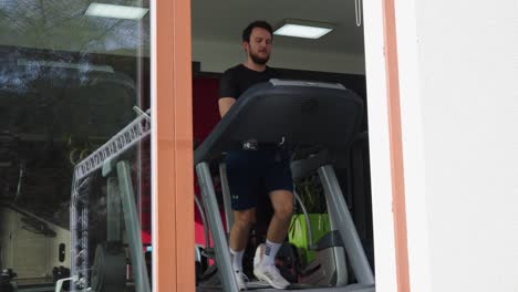 Vista-Desde-El-Exterior-Del-Gimnasio-A-Través-De-La-Ventana-De-Un-Hombre-Corriendo-En-Una-Cinta-De-Correr