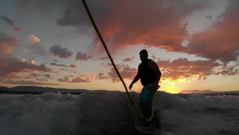 Silhouette-slo-mo-wave-surfer-behind-boat-with-colorful-orange-sunset