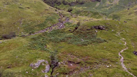 Aerial-shot,-tracking-and-panning-along-a-Hiking-trail-on-the-lush,-green-valley-hillside-of-Glen-Coe,-Scotland