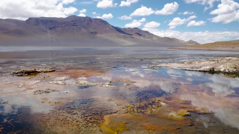 Landscape-with-mountains-in-the-back-and-lake-with-small-geyser-in-front,-Atacama-desert,-Chile