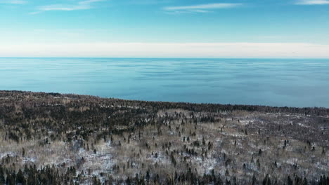 aerial-drone-view-flying-over-green-snowy-forest-in-winter-away-from-shoreline-of-blue-lake-superior-in-winter-in-northern-minnesota