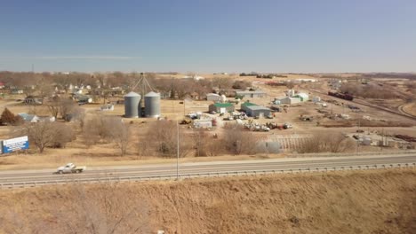 Vista-Aérea-De-La-Campiña-Del-Medio-Oeste-Americano,-Autopista-Por-Silos-De-Almacenamiento-De-Granos-Bajo-El-Sol-De-Primavera,-Falls-City,-Nebraska,-EE.UU.