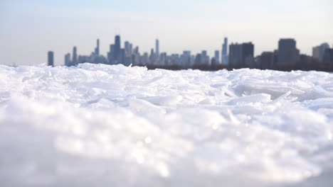 Schwenken-Vorbei-An-Einem-Riesigen-Haufen-Gefrorenen-Seeeises-Im-Vordergrund-Mit-Der-Unscharfen-Skyline-Von-Chicago-Im-Hintergrund