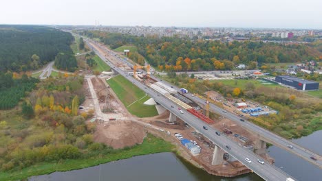 Industrial-cranes-constructing-bridge-over-Neris-bridge-in-Kaunas-city,-aerial-panoramic-view