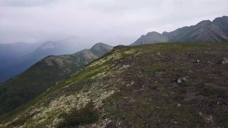 Hiker-Boy-Walks-Along-Mountain-Ridge-in-Alaska-while-Drone-Flies-By