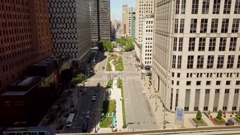 4k-aerial-footage-of-detroit-people-mover,-city-streets,-unrecognizable-people,-in-the-summer-time-outdoors-on-a-sunny-day-with-pale-blue-sky