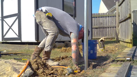 Man-aims-water-hose-at-hands-an-a-post-hole