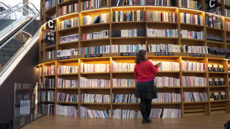 Mujer-Caminando-Junto-A-Una-Estantería-Y-Tomando-Un-Libro-En-El-Centro-Comercial-Coex-De-La-Biblioteca-Starfield-En-Seúl,-Corea-Del-Sur