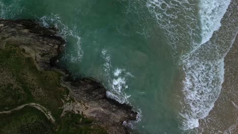 Vista-Aérea-De-Arriba-Hacia-Abajo-Sobre-Una-Playa-En-Cornwall-Con-Olas-Del-Océano-Rompiendo-A-Lo-Largo-De-La-Costa-Rocosa,-Reino-Unido