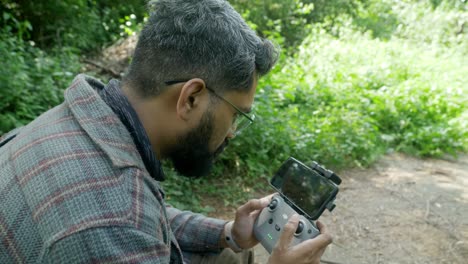 Professioneller-Drohnenpilot-Verwendet-Drohnenfernbedienung-Mit-Einem-In-Einer-Waldlandschaft-Befestigten-Smartphone