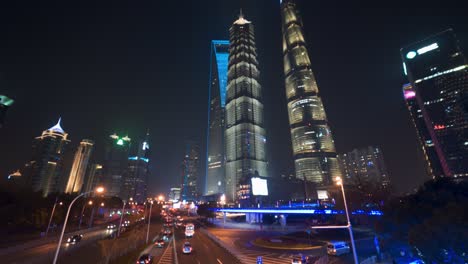 Infraestructura-Vial-Por-La-Noche-Con-La-Plaza-De-Las-Torres-De-Shanghai-Iluminada,-Toma-Panorámica