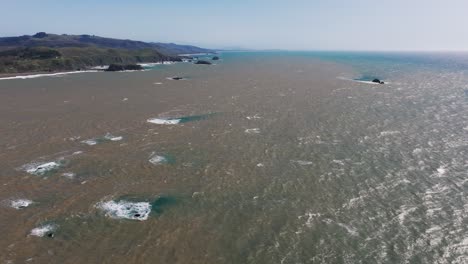 Drone-aerial-shot-of-brown-and-dirty-water-mixing-with-ocean-water-off-the-pacific-coast