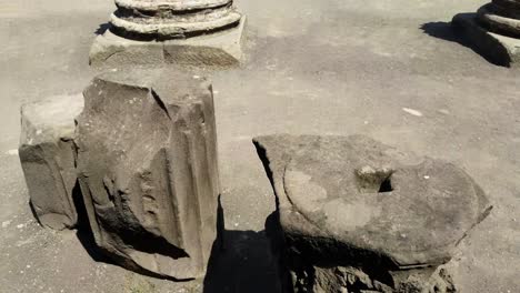 Tilt-up-of-the-camera-showing-the-ruins-of-one-of-the-central-areas-of-the-city-of-Pompeii,-with-some-tourists-visiting-it-during-a-sunny-summer-day