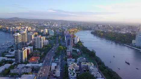 Panning-aerial-view-of-a-city-with-busy-street,-river-and-tall-buildings-in-the-evening