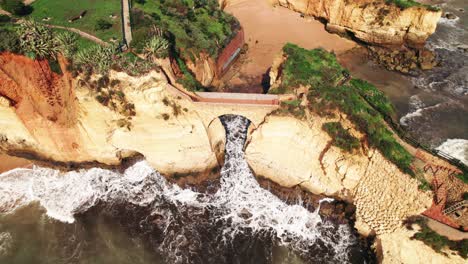 Vista-Aérea-Ascendente-De-Drones-4k-Del-Arco-Artificial-En-La-Playa-Estudantes-Con-La-Ciudad-De-Lagos-Apareciendo-En-La-Región-Del-Algarve-De-Portugal