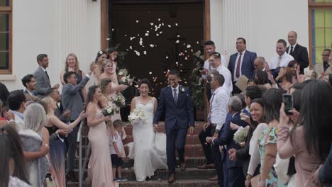 Young,-mixed-race-wedding-couple,-just-married,-exiting-the-church-and-greeted-with-the-throwing-of-confetti-by-family-and-friends-in-slow-motion