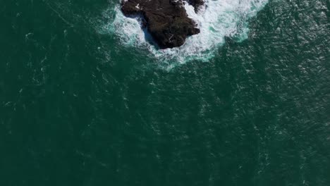 Vista-Aérea-De-Drones-Mirando-Hacia-Una-Isla-Rocosa-Mientras-Las-Olas-Rompen-Sobre-Ella