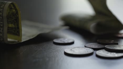 Camera-pan-right-over-US-currency,-various-coins-in-the-foreground-with-one-dollar-bills-in-the-background-in-natural-light