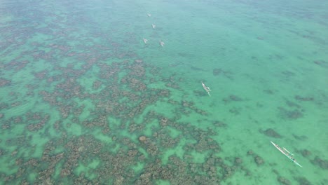 drone-footage-across-the-shallow-reef-filled-water-near-Lanakai-beach-Oahu-Hawaii-with-Hawaiian-outrigger-canoes-paddling-across-the-clear-turquoise-water