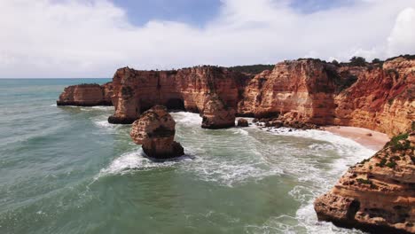 Coastline-pan-down-view-with-beautiful-orange-rugged-cliffs-by-aerial-4k-drone-at-Ponta-da-Piedade-near-Lagos-in-the-Algarve-region-of-Portugal