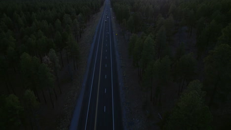 Aerial-View-of-Straight-Road-Traffic-Between-Conifer-Woods-in-Countryside-of-USA-in-Twilight,-Revealing-Drone-Shot