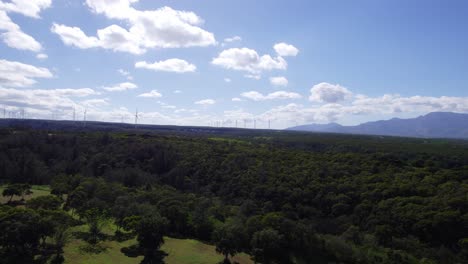 Drohnenaufnahmen-In-Der-Nähe-Der-Nordküste-Von-Oahu,-Hawaii,-Mit-üppigen-Grünen-Bergen-Und-Windmühlen-Für-Ökostrom-Am-Horizont